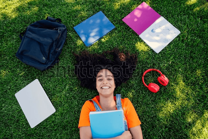 A happy girl laying on the grass surrounded by school supplies